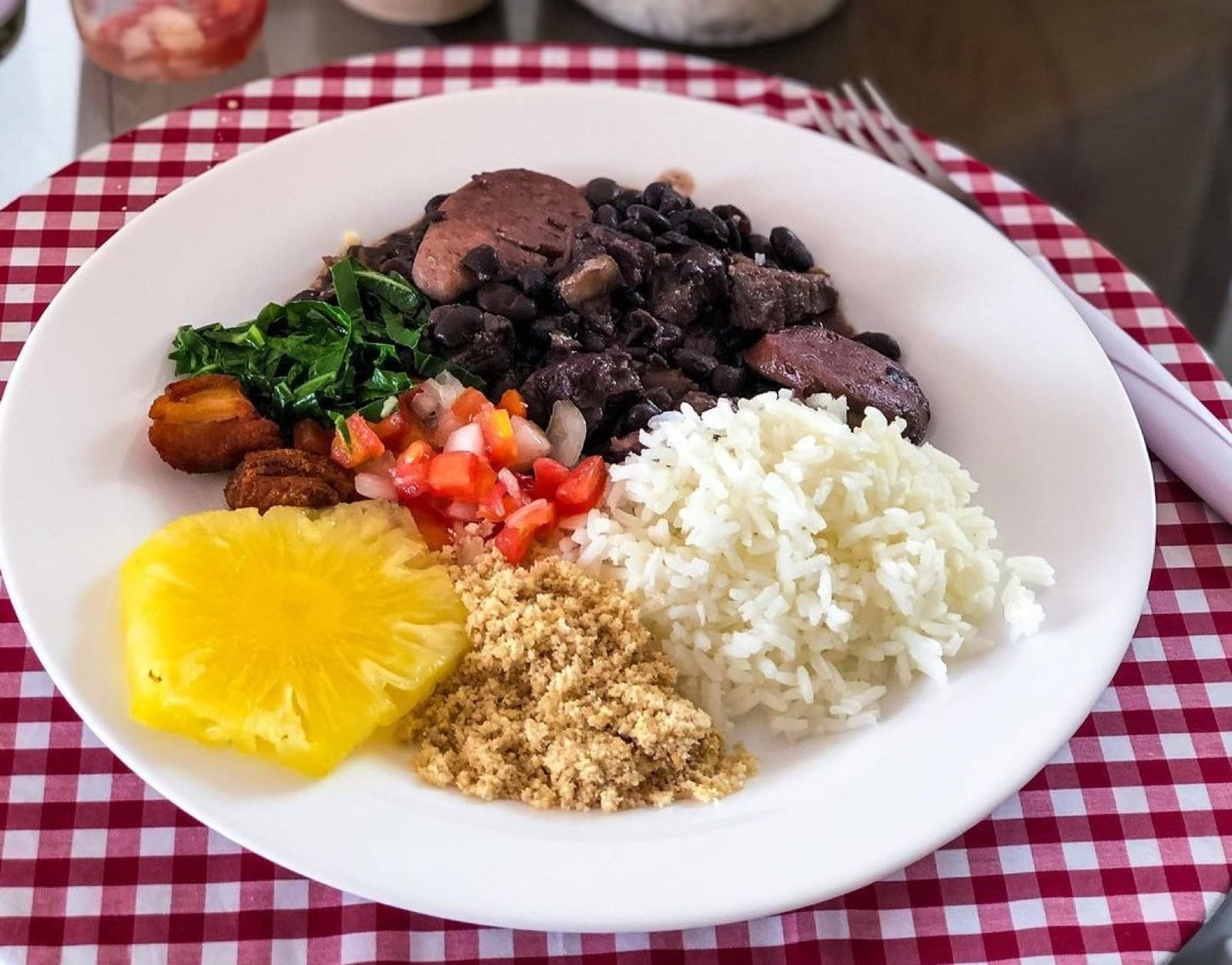 A plate of feijoada with rice, farofa, collard greens and vinaigrette
