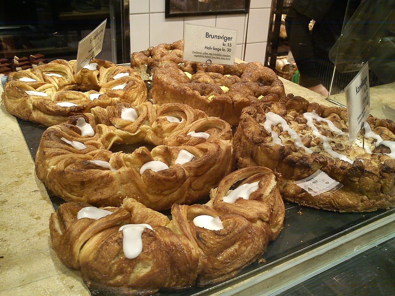 Kringle and other wienerbrød laid out with their prices in a Danish bakery window