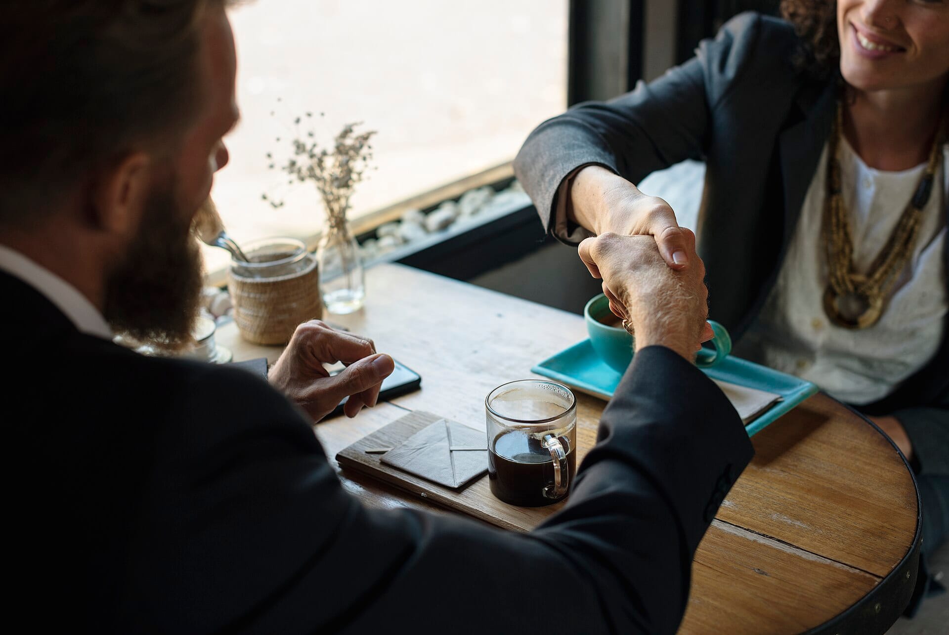 Two people shaking hands across a cafe table