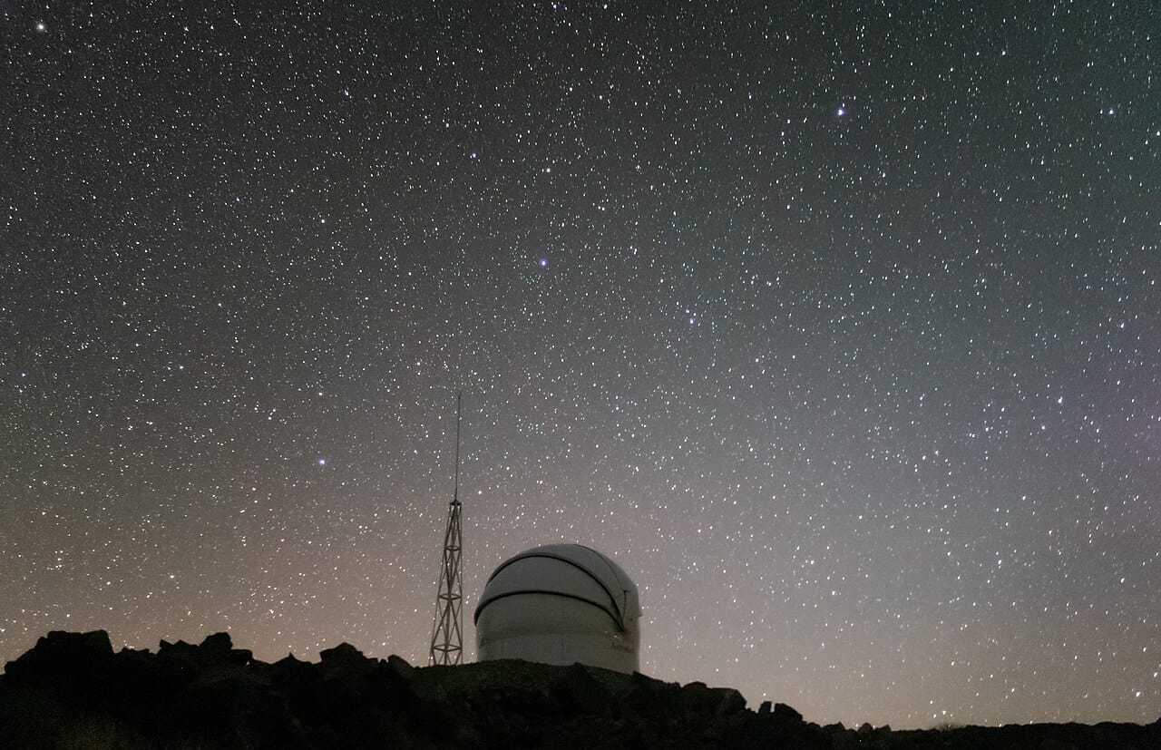 An observatory dome on a ridge under a sky thick with stars