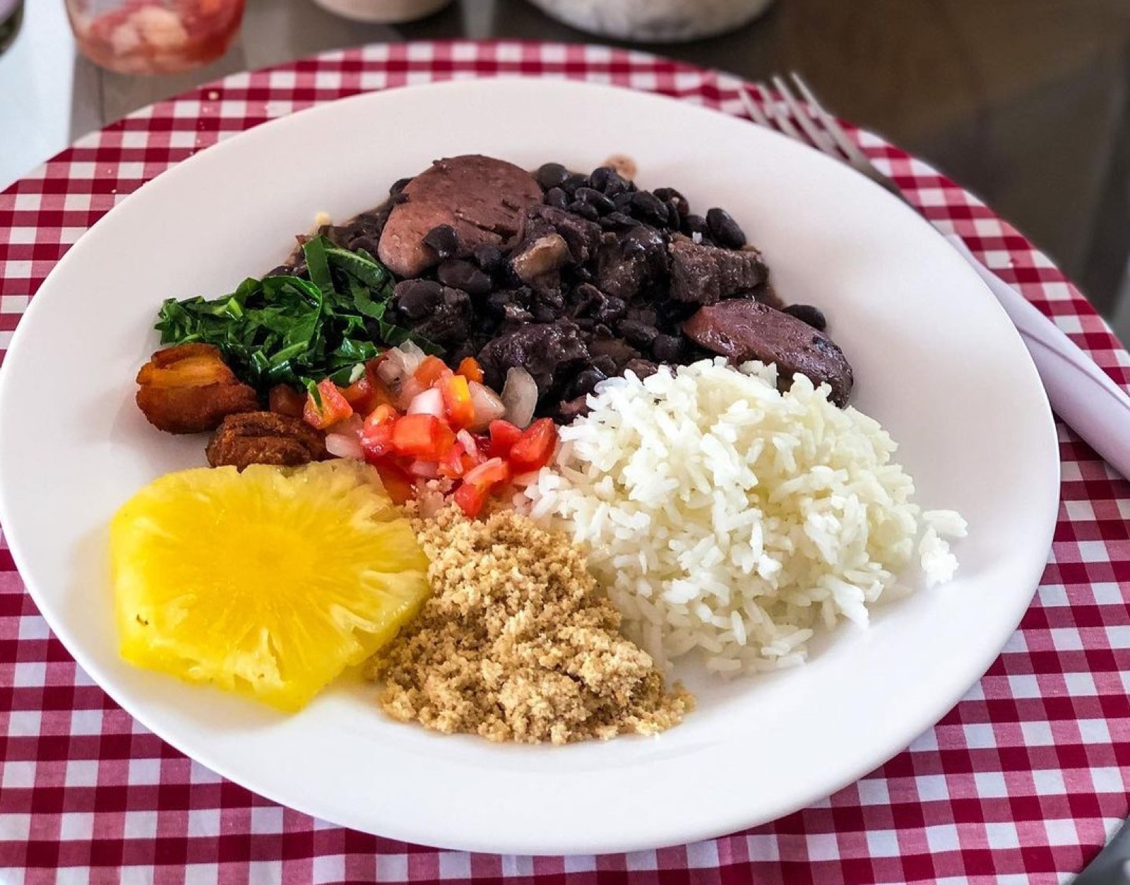 A plate of feijoada with rice, farofa, collard greens and vinaigrette