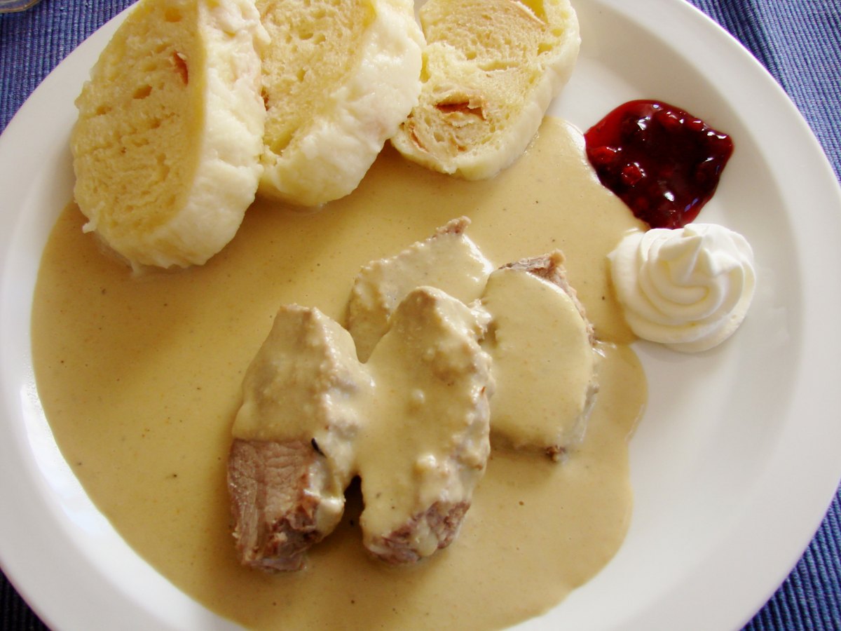 Svíčková na smetaně served with sliced bread dumplings and cranberry garnish