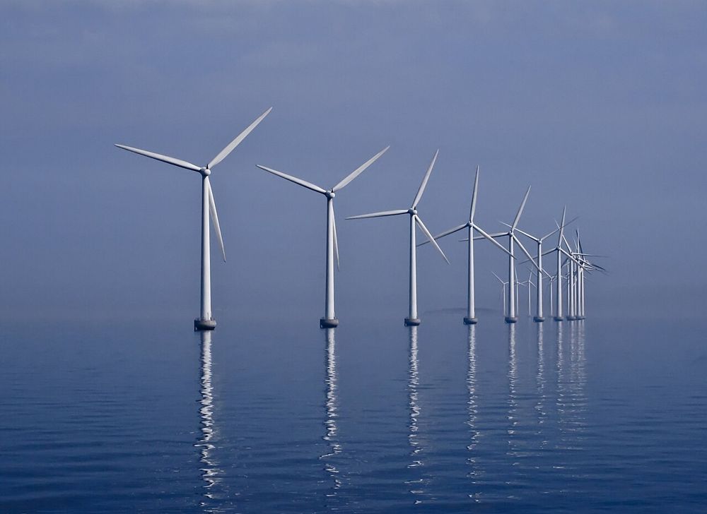 A row of white offshore wind turbines standing in calm water