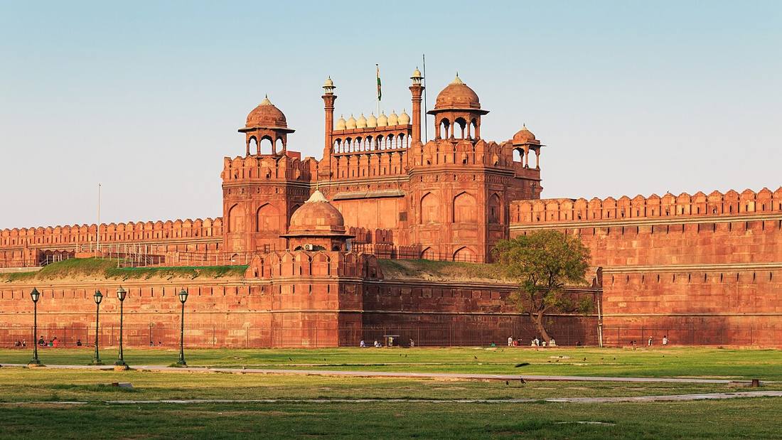 The red sandstone walls and domed pavilions of the Red Fort over a green lawn