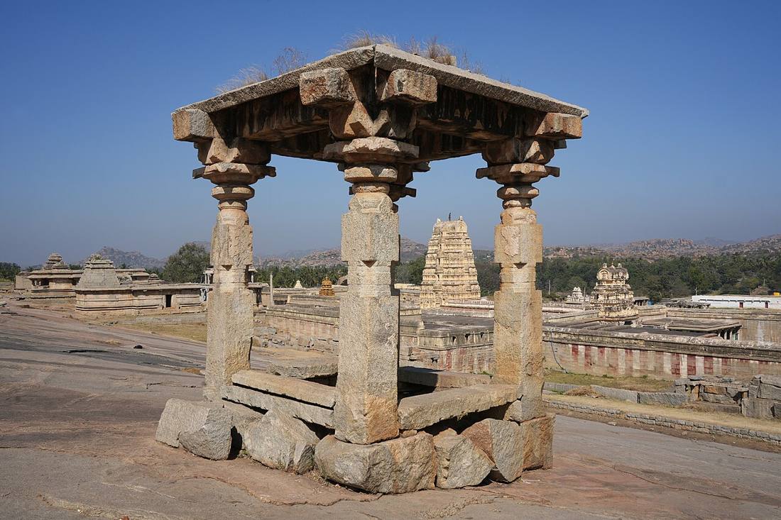 A stone pavilion on Hemakuta Hill with the tower of the Virupaksha Temple behind