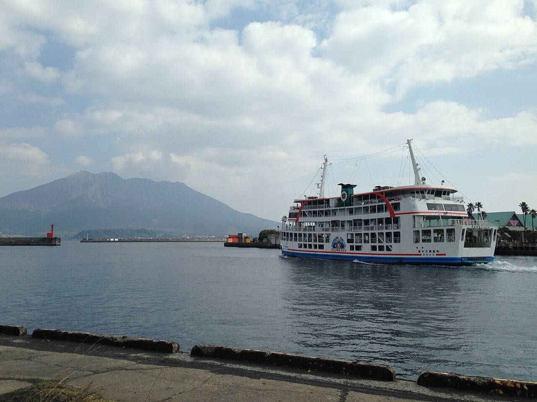 A white Sakurajima ferry crossing the bay with the volcano behind it