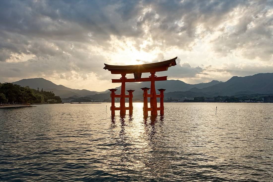 The great orange torii of Itsukushima standing in calm water at sunset