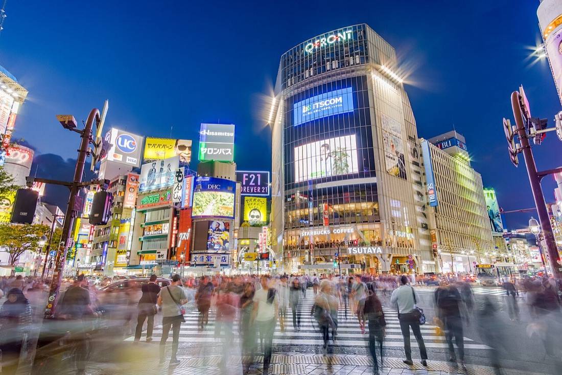 Crowds crossing Shibuya’s scramble at dusk under giant lit screens