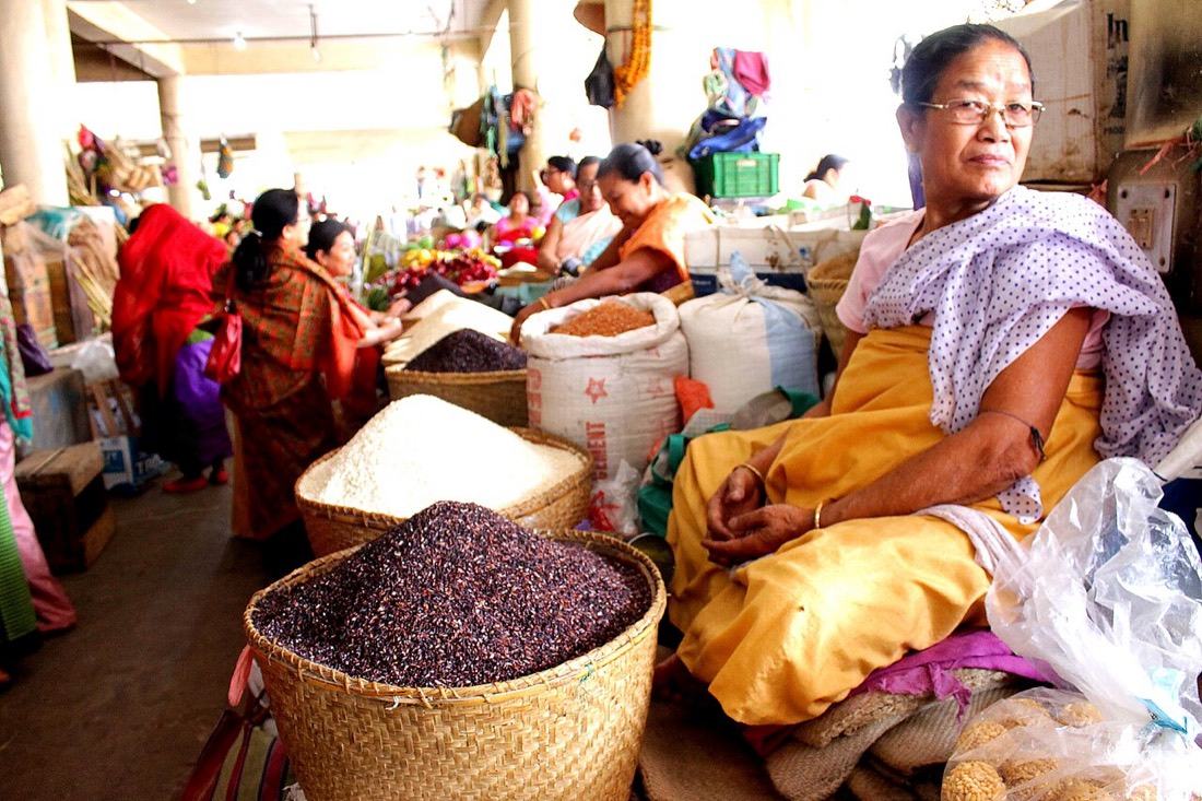 A woman trader at Ima Keithel beside baskets of black and white rice