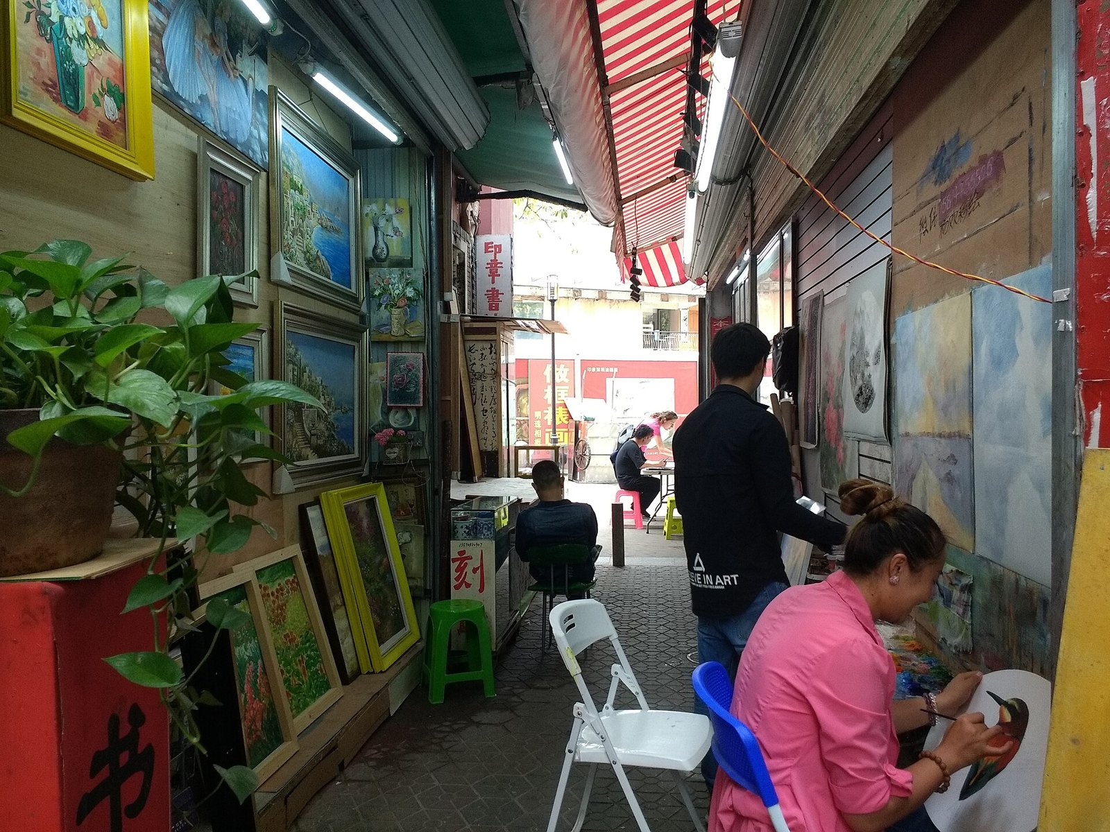 Artists painting canvases at work in Dafen Oil Painting Village