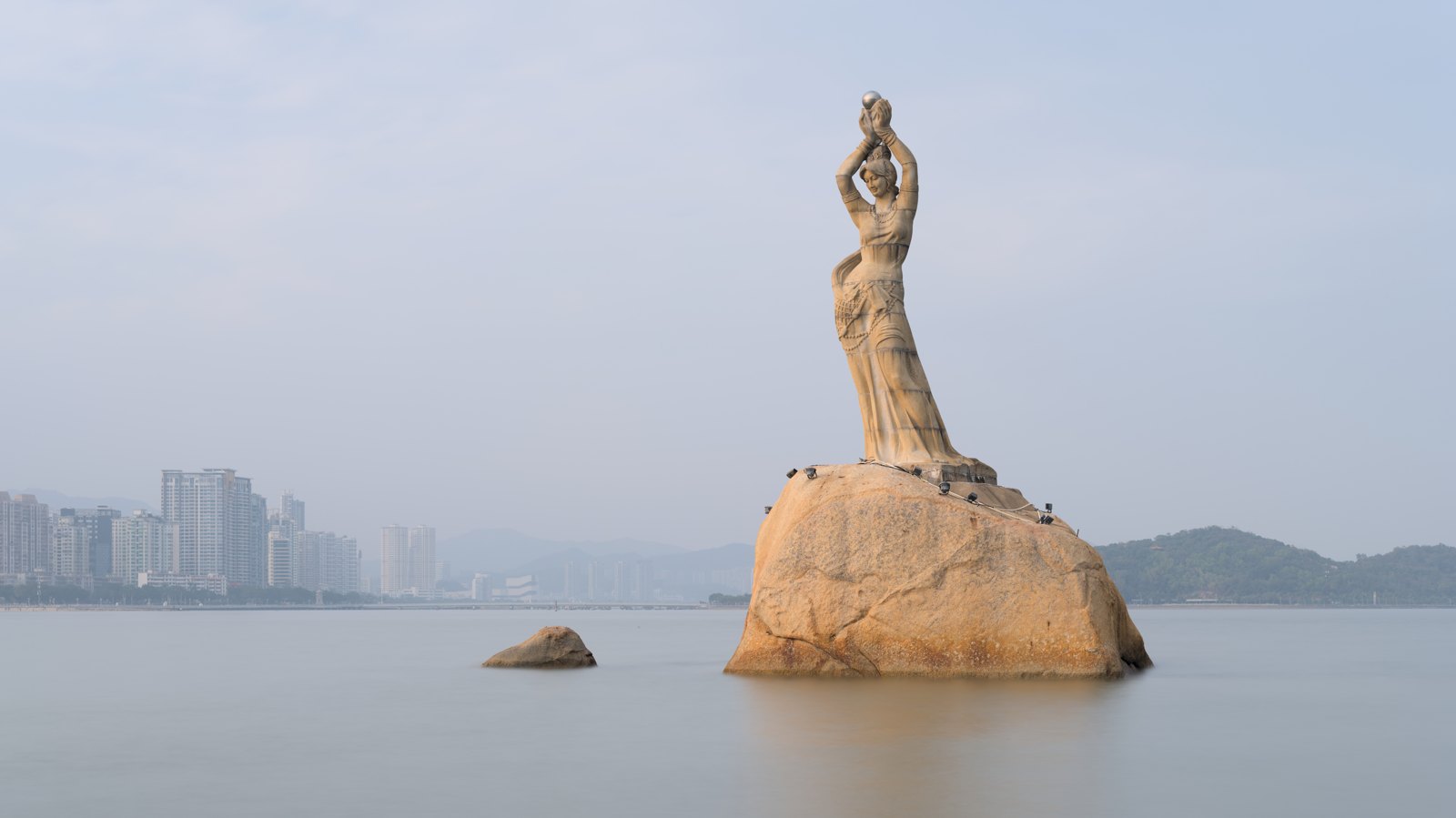 Zhuhai’s Fisher Girl raising a pearl above her head on a rock in the bay