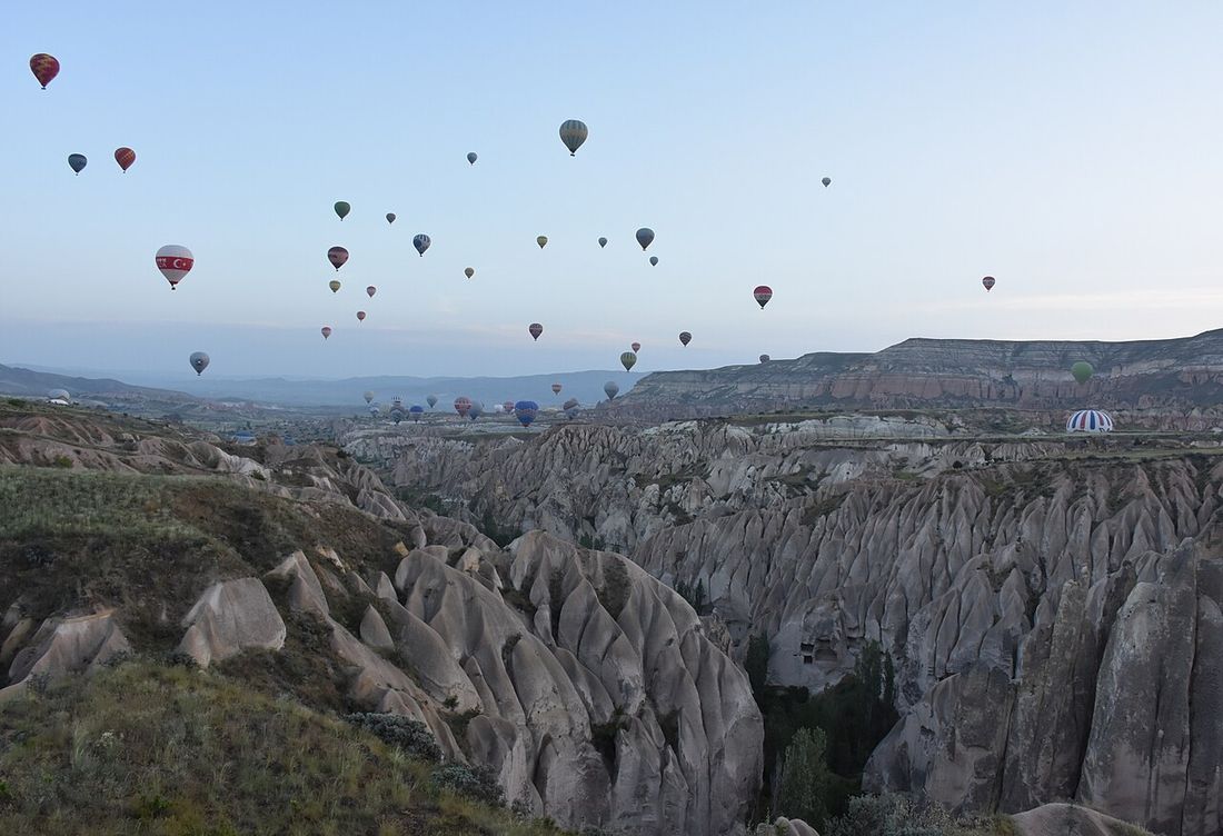 Dozens of hot air balloons rising at dawn over the rock pinnacles of a valley near Göreme