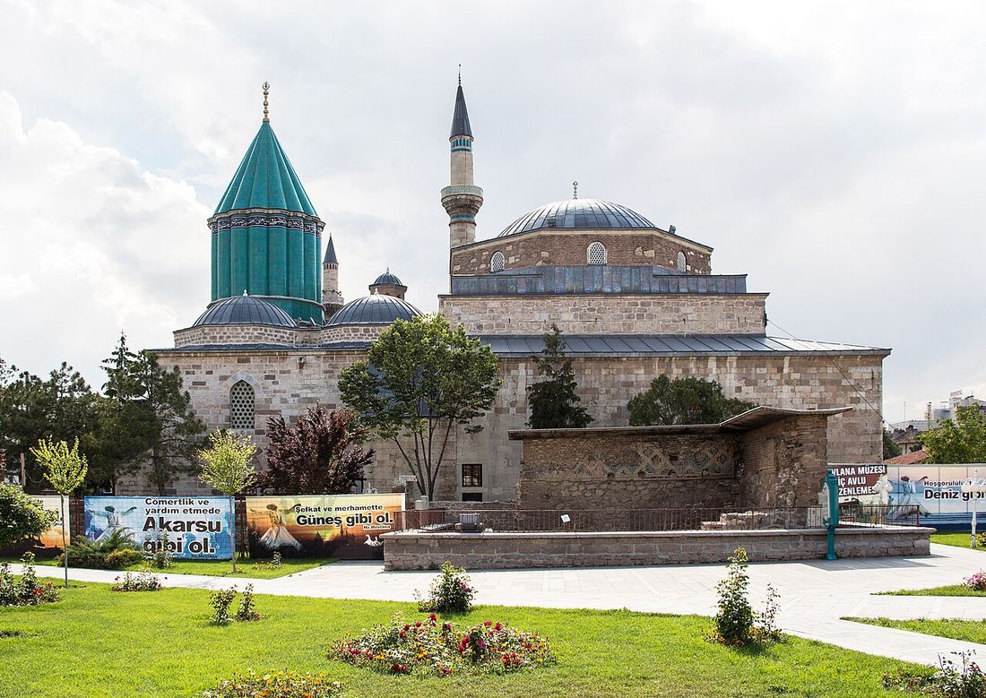 The green-tiled dome and minaret of the Mevlana Museum in Konya behind a garden of lawns and flowers