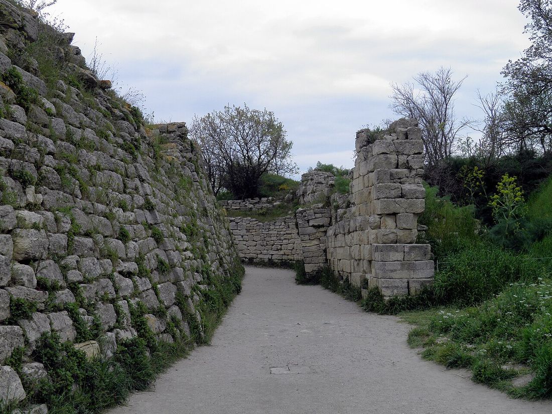 A path running between the sloping stone walls of ancient Troy, overgrown with trees