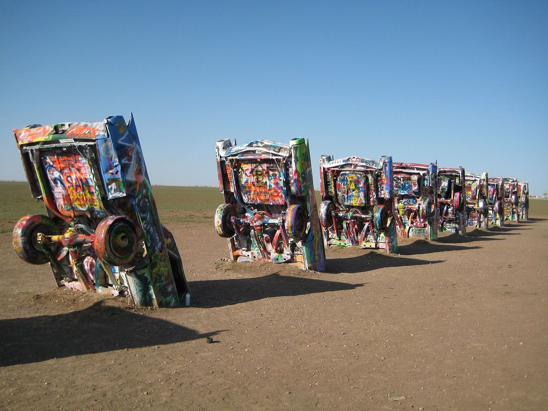 A row of spray-painted Cadillacs buried nose first in a dry Texas field