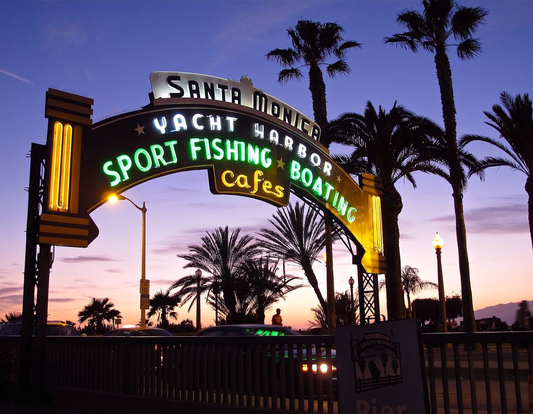 The neon arch over the entrance to Santa Monica Pier at dusk, framed by palm trees